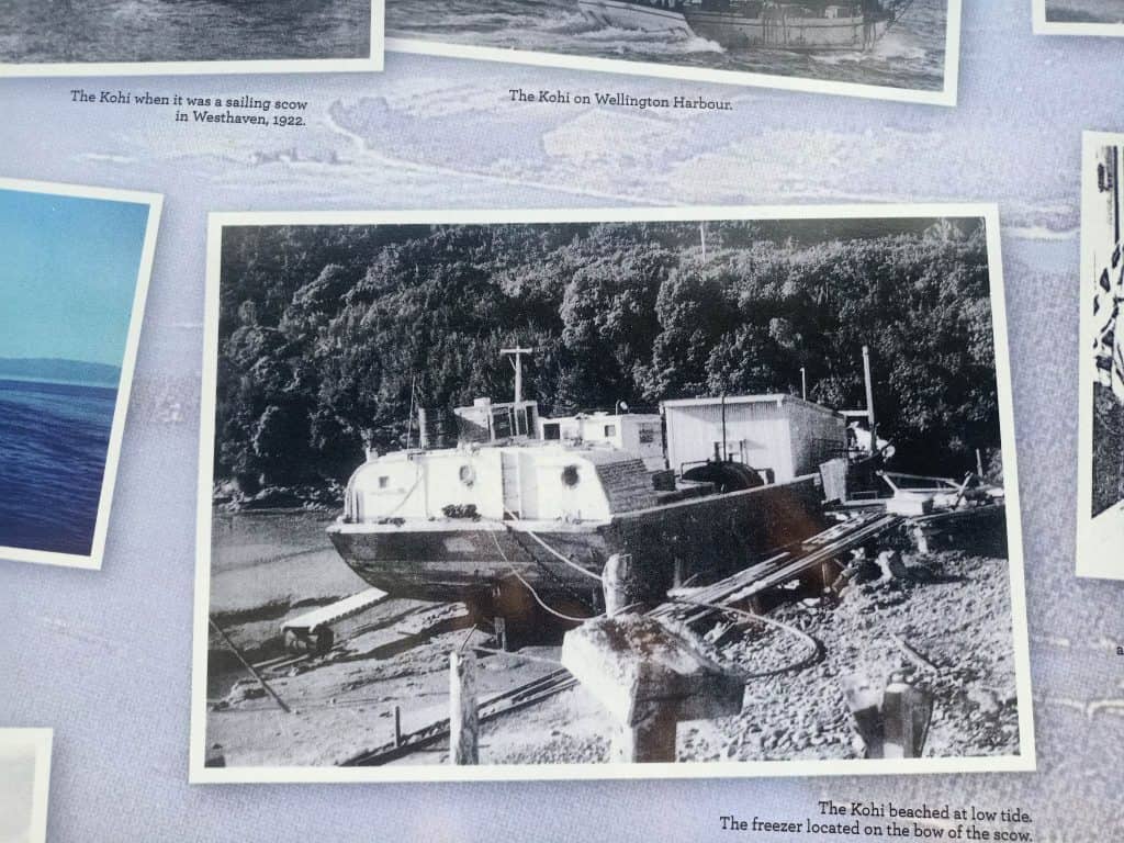 Image of Kohi beached at low tide whilst still in use. The photo is reproduced on a panel at Mangarākau Wharf