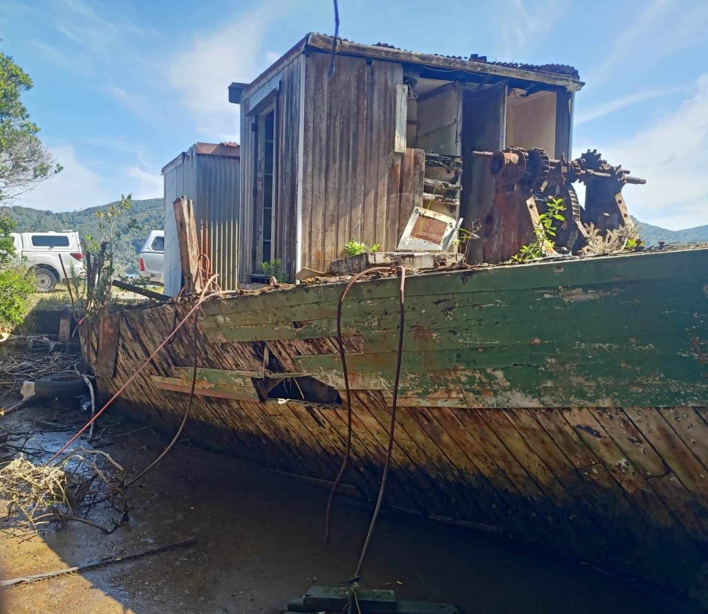 Close up view of Kohi, a wooden scow. The boat is beached and is in disrepair.