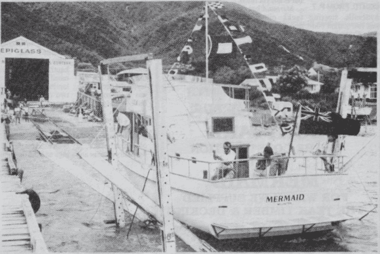 Black and white image of a boat called Mermaid on a slipway trolley.  The boat has flags tied to its mast.  The image cam from a newspaper article.