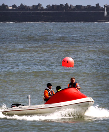 View of a jet boat with three crew moving through the water.  A red float in the water behind the boat marks where the Noelene sunk in 2011