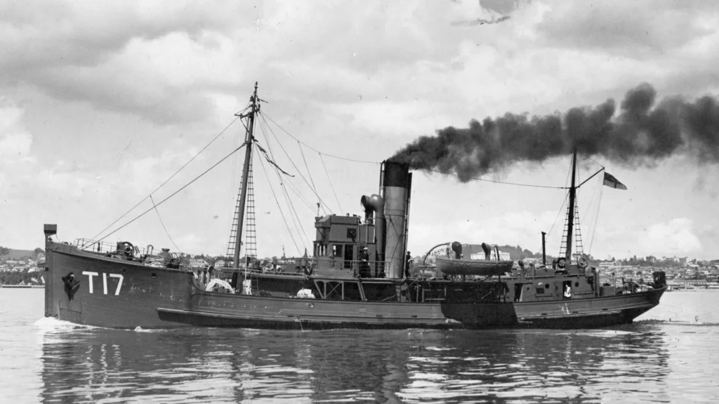 Black and white image of the minesweeper Hinau seem side on with smoke billowing out of her stack.