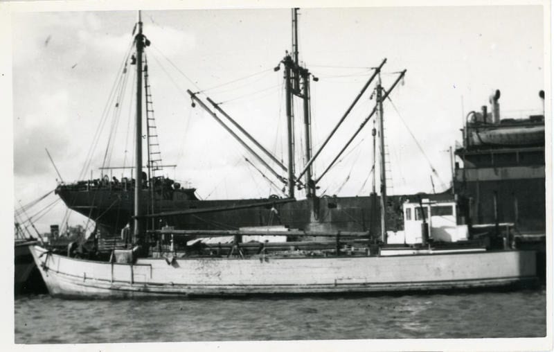 Black and white photograph of scow Vesper alongside wharf. Seen from the side with her sails down.