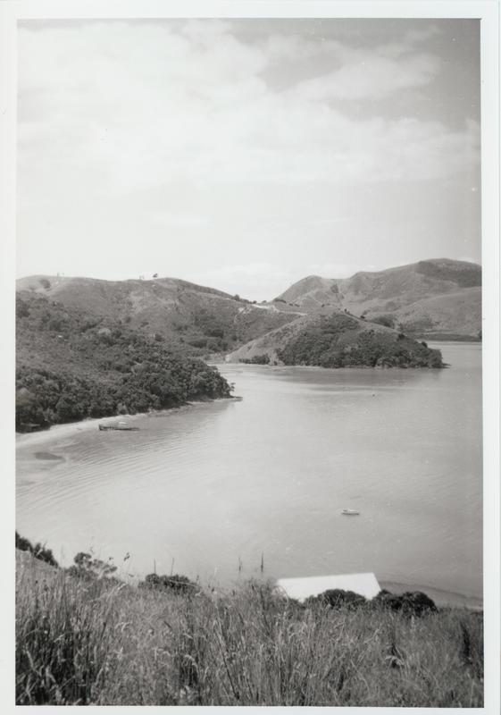 Black and white image of a bay seen from uphill. Boats can be seen in the water and one is on the beach.